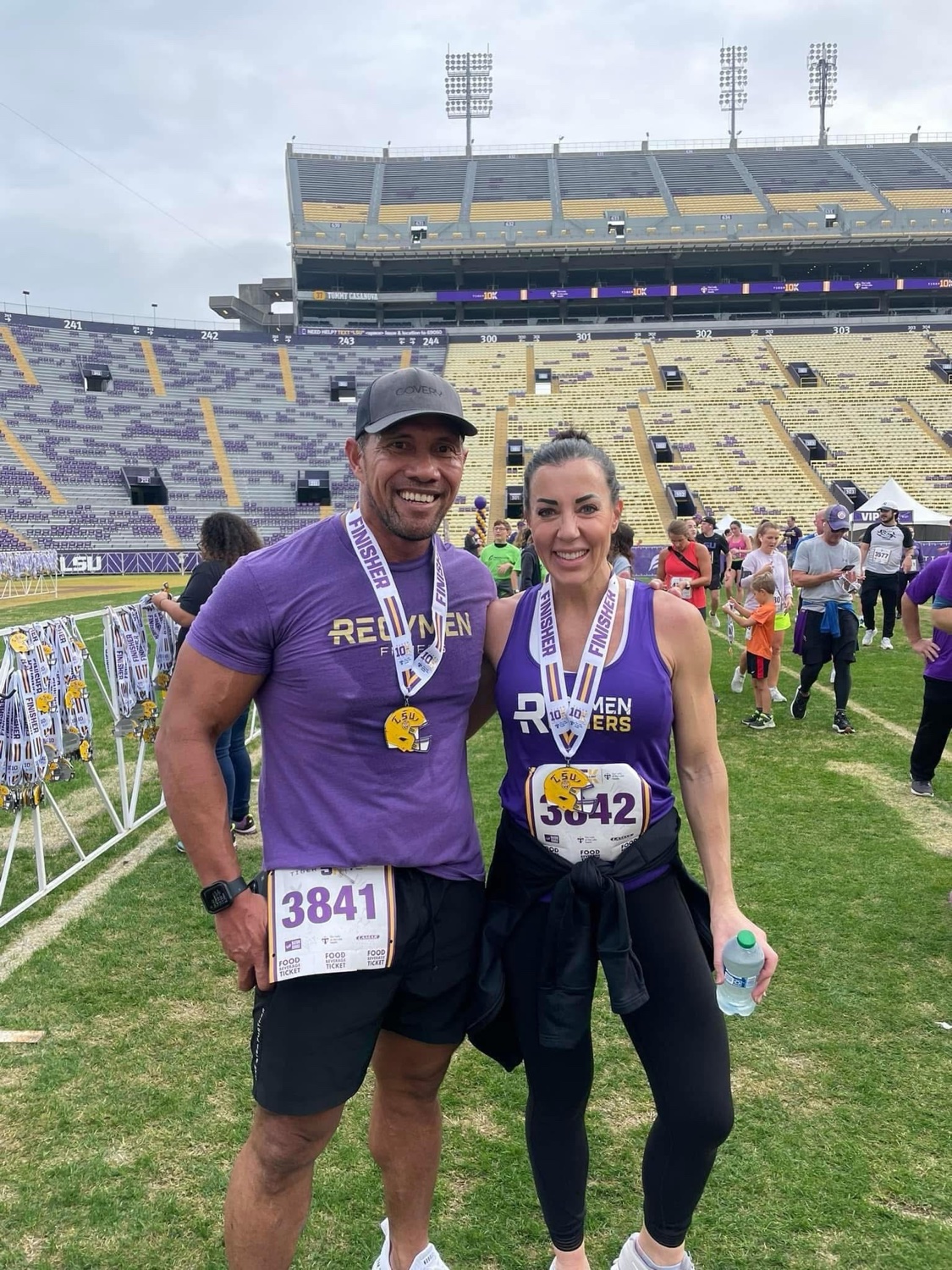 Coach Laie and Head Coach Emily Wong on the field at LSU Tiger Stadium with finisher medals, wearing Regymen gear